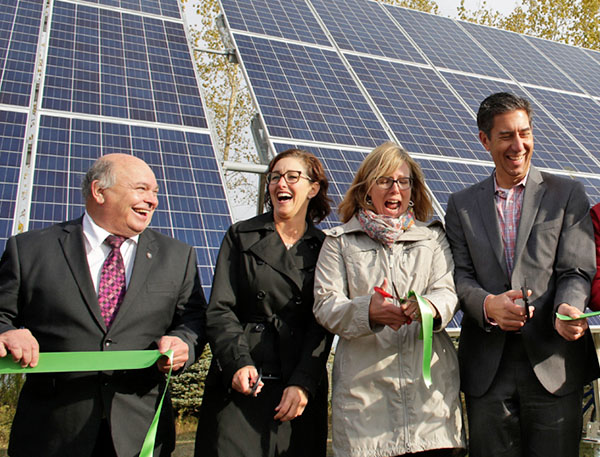 FortWhyte Alive Solar Array Four people cutting a green ribbon in front of an array of solar panels. They are smiling and laughing.