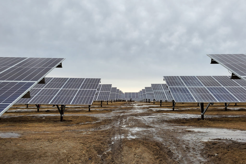 Low angle photograph of rows of solar panels in a winter landscape on a cloudy day.