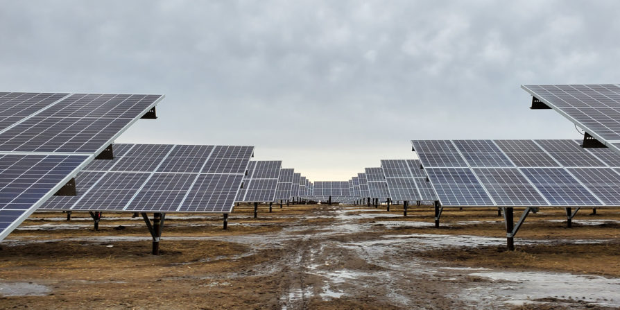 Low angle photograph of rows of solar panels in a winter landscape on a cloudy day.