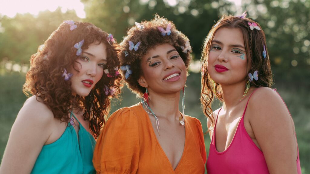 Three models wearing Cheekbone Beauty makeup, bright clothing, and butterfly accessories.