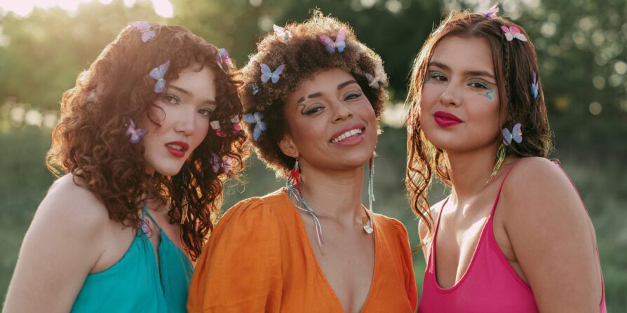 Three models wearing Cheekbone Beauty makeup, bright clothing, and butterfly accessories.